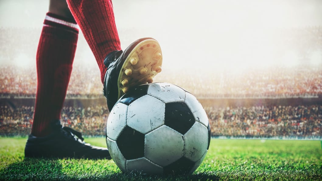 Jogador com o pé sobre a bola de futebol no gramado de um estádio
